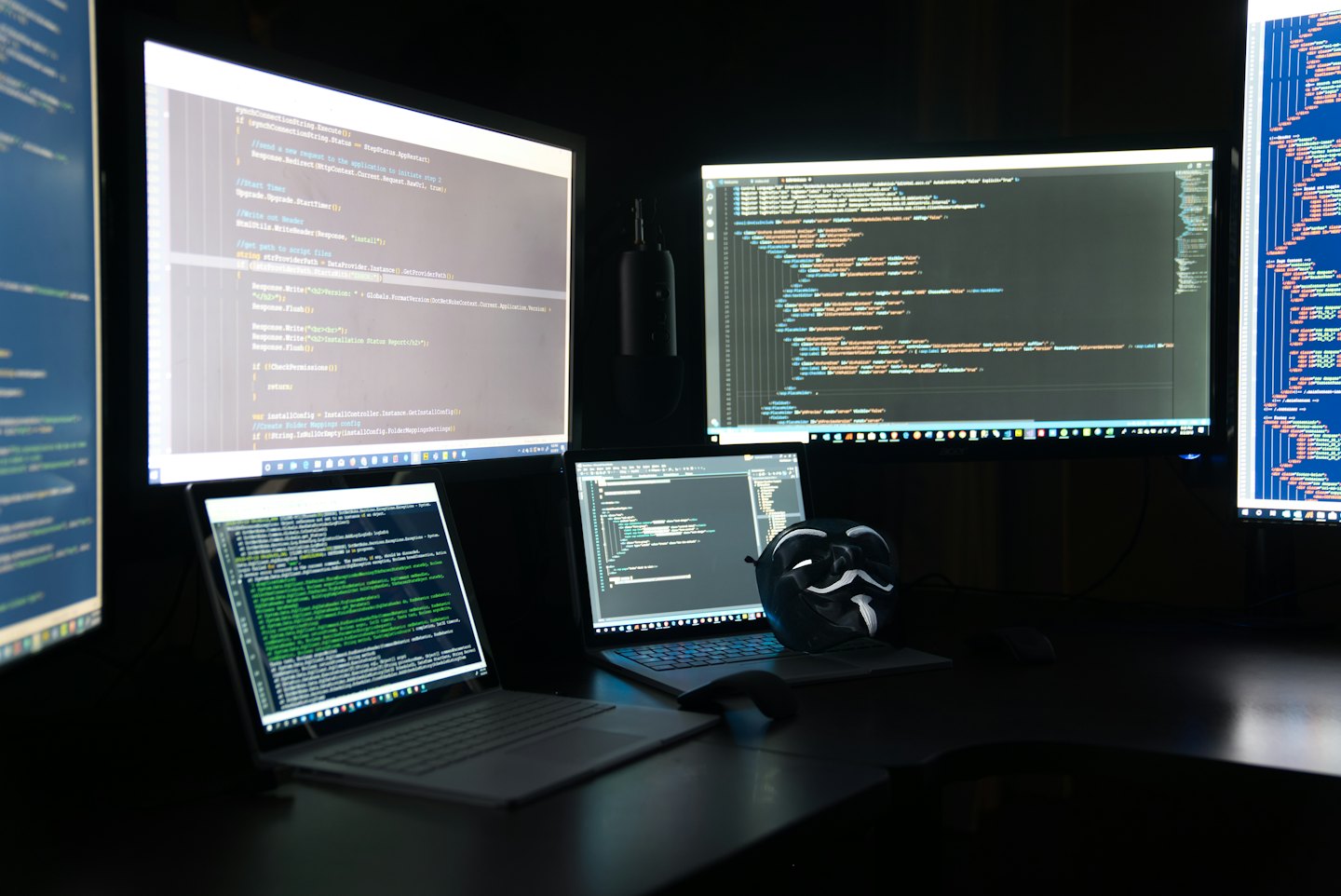 Una maschera di Guy Fawkes appoggiata su una tastiera tra più monitor.